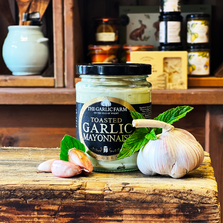 This is a lifestyle image of the tasted Garlic mayonnaise on a wooden board surrounded by garlic bulbs