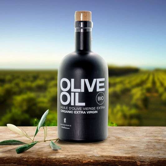 Black Olive Oil bottle sat on a table in front of a olive field