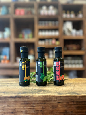 Image shows three of the Jorges oils. Blood orange, lime and lemon on a wooden block in a farm shop setting.