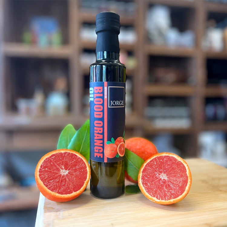 The glass of Blood Orange oil bottle in the Jorge's shop. In the image the Blood Orange oil bottle is on a block of wood with Blood Oranges resting on the bottle.