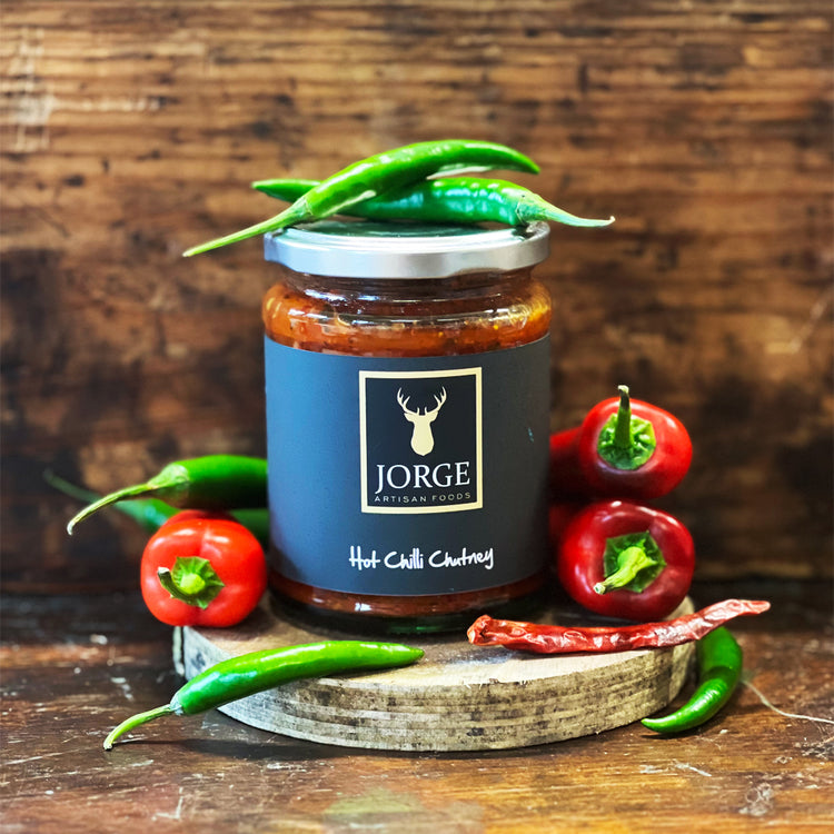 Jar of Jorge Hot Chilli Chutney with red chillies on a table