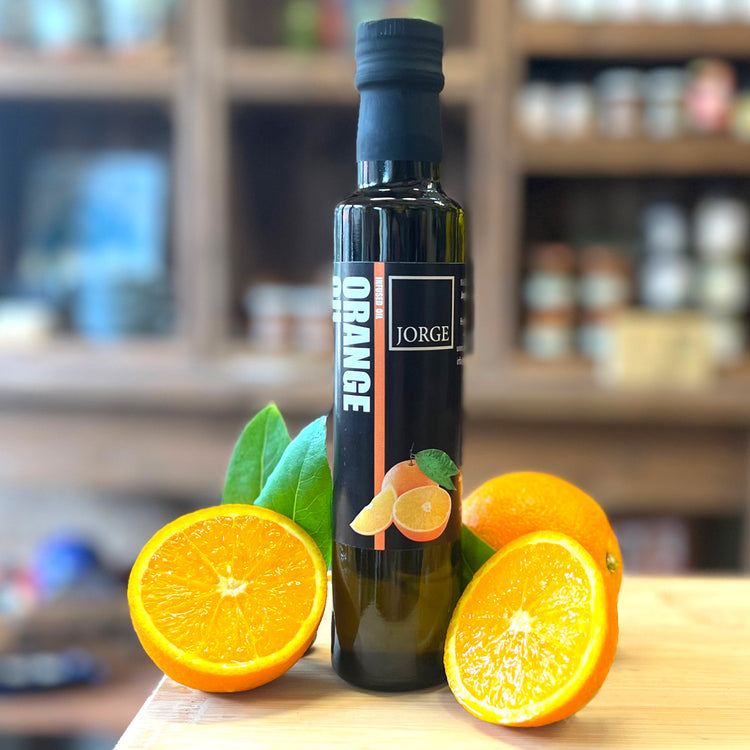 The glass of Orange oil bottle in the Jorge's shop. In the image the Orange oil bottle is on a block of wood with Oranges resting on the bottle.