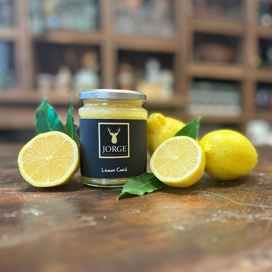 Lemon curd in a lifestyle setting. The jar is surrounded by lemons, and the jar has black Jorge's branding with the label saying lemon curd