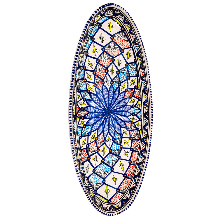 An oval ceramic dish with a colorful kaleidoscope pattern. The design features a central blue flower surrounded by intricate shapes in shades of red, pink, yellow, and blue. The border of the dish is decorated with a wavy line.