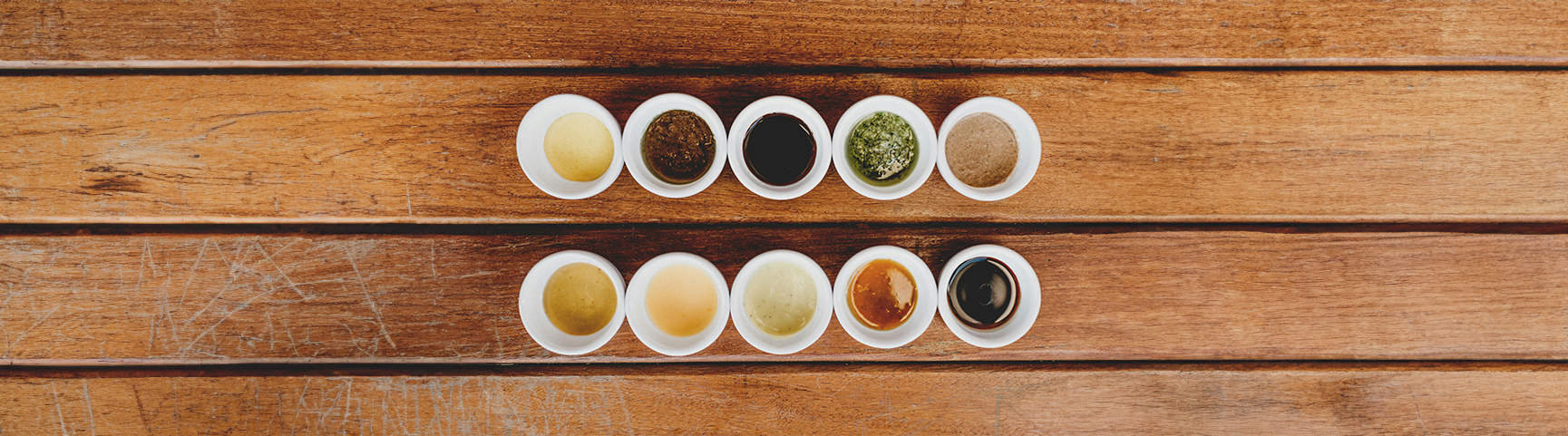 A selection of various sauces and dressing in small dipping dishes displayed on a wooden table