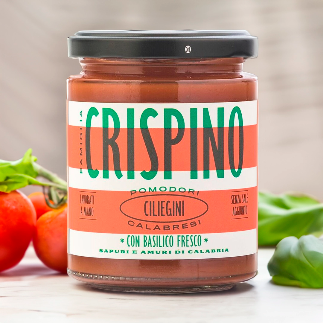 Crispino cherry tomatoes jar on table surrounded by fresh tomatoes and fresh basil