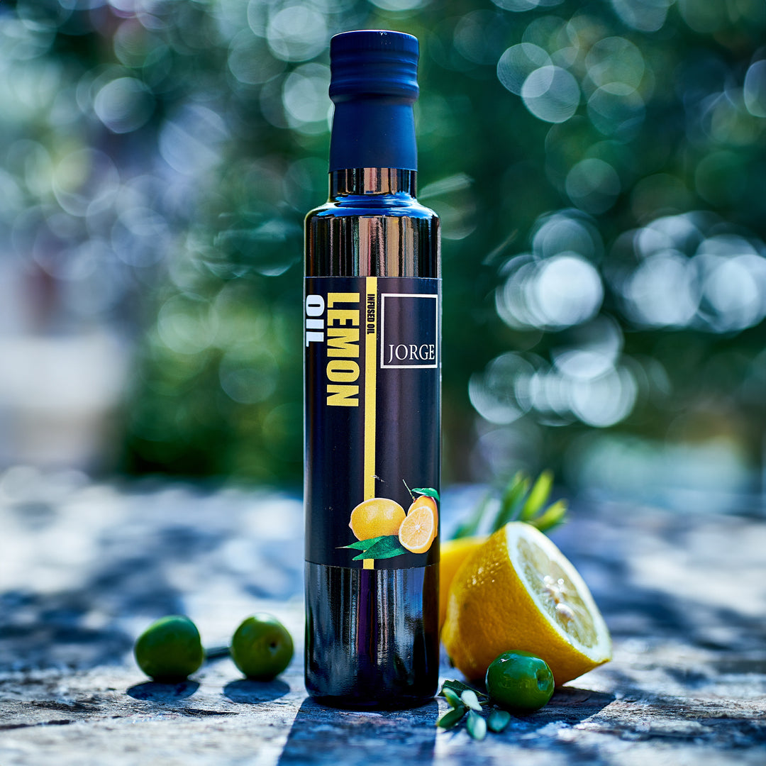 Jorge Lemon infused extra virgin olive oil for summer dining. Image in an alfresco setting with bottle of lemon oil and lemons in the surrounding 
