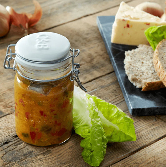 Cartwright & Butler Piccalilli jar on a wooden table with a cheeseboard and lettuce in the background.