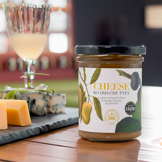 A glass jar with Cheese Board Chutney written on with the Kew Gardens logo. In a lifestyle setting with cheese on a cheeseboard.